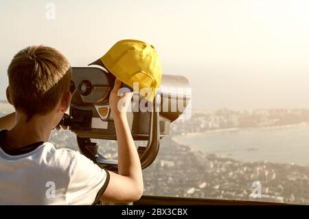 Young boy looking through a coin operated binoculars on the Gelendzhik from a mountain nearby. Toned. Stock Photo