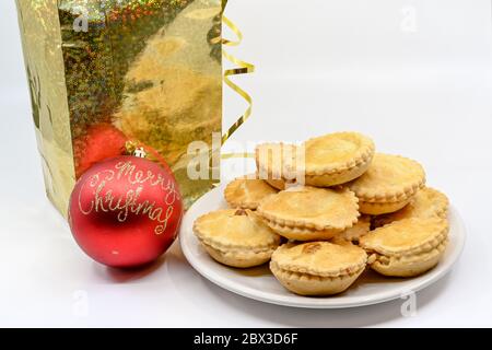 Mince pies on a white plate, with a Merry Christmas bauble and a gold gift bag Stock Photo