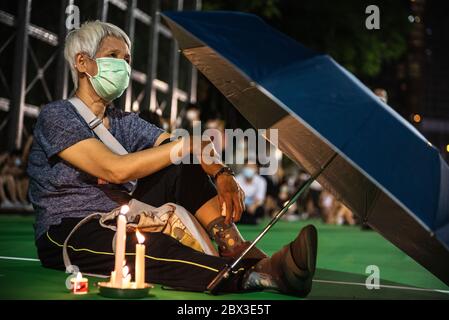 A woman protects her burning candles from the wind using an umbrella during the anniversary rally.Thousands of Hong Kong residents attended a rally commemorating the 31st anniversary of the Tiananmen Square Massacre. Rally attendees chanted slogans, lit candles and held a moment of silence in remembrance of the day. Stock Photo