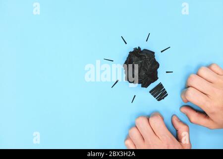 Black light bulb crumpled paper in blue background with hands flat lay. Blank, dim mind and lack of creativity. Stock Photo