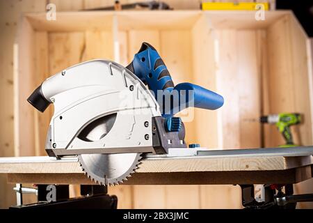 hand circular saw with piece of wood on workbench. closeup of sawing machine woodworking construction tool concept furniture making diy background Stock Photo