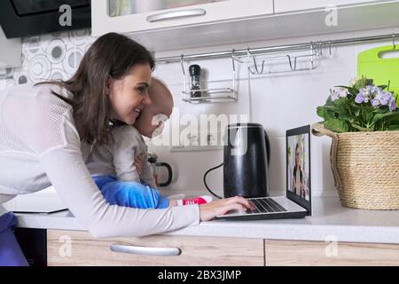 Young woman with toddler in her arms making video call using laptop at home Stock Photo