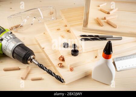 wooden dowel joint pins drill glue wood planks safety glasses cordless screwdriver and tools on spruce background. Carpenter industry funiture making Stock Photo