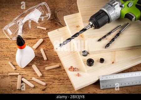 wooden dowel joint pins drill glue wood planks safety glasses cordless screwdriver and tools on rustic oak background. Carpenter industry funiture mak Stock Photo