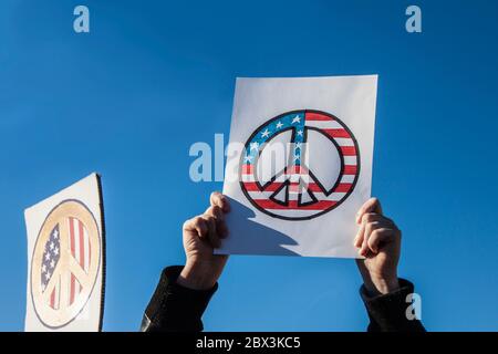 Mans hands holding up hand drawn peace sign against blue sky with another peace sign blurred behind him Stock Photo