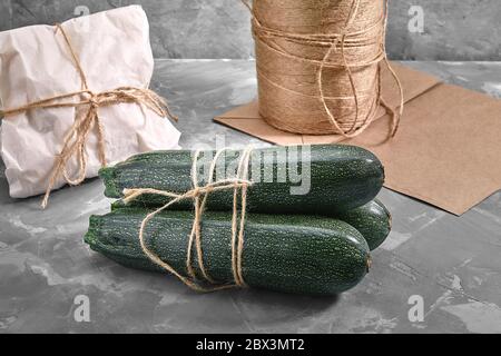 A bunch of zucchini on a gray background with a paper bag for delivery, food delivery, environmental packaging. Copy space, fresh vegetables. Stock Photo