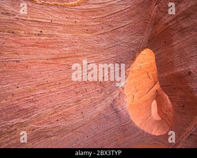 A red-brown rock face with rough lines and a small opening Stock Photo