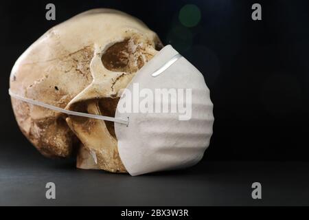 Isolated skull against a plain dark, black background wearing a simple paper mask for protection against smell fumes disease or virus. Covid-19 corona Stock Photo