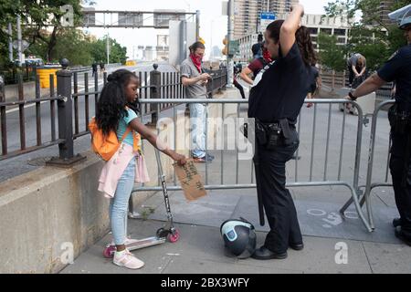 New York, New York, USA. 4th June, 2020. A young girl asks a New York City Police officer about her helmet during a Justice for George Floyd protest and rally on the Brooklyn Bridge in New York, New York. Tens of thousands of people protested across the United States and in major world cities for another night of outrage over police brutality intensified over the death ofÂ George Floyd. Credit: Brian Branch Price/ZUMA Wire/Alamy Live News Stock Photo