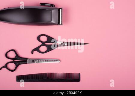 hair clipper, straight and thinning barber scissors and comb on a pink background top view, copy space. hairdressing tools. Stock Photo