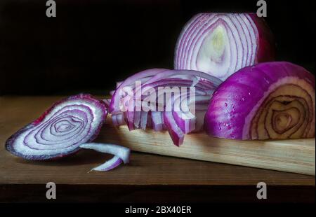 slices of purple onion on a cutting board in black background, using the chiaroscuro technic, or low key light for dark food photography. Stock Photo