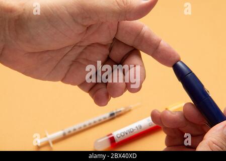 person doing fingertip test for blood glucose, with vacuum tube for blood testing of test blood with covid-19 label Stock Photo