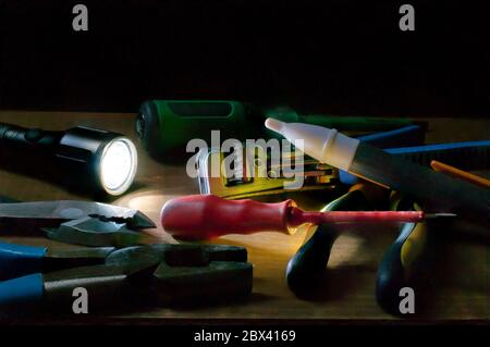 Electricians tools in a dark place lit by a flashlight, screwdriver pliers wire strip, voltage detector on a table. Stock Photo