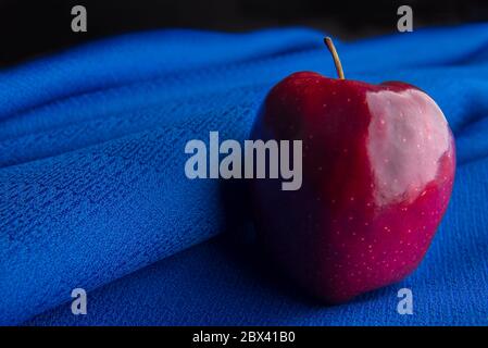 still life photography, Red apple on a blue tablecloth in a dark background. low key light or dark food macro photography. Stock Photo