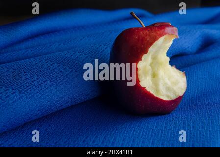 low key light or dark food photography. bitten red apple on a blue tablecloth. Still life Stock Photo