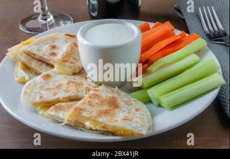 Dipping a quesadilla in ranch dip with celery and carrots sticks on a sampler plate