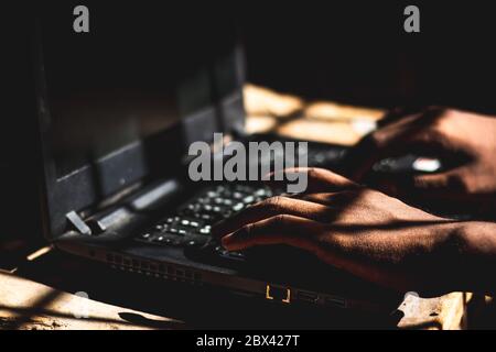 The Hacker using his laptop computer to open Dark web sites at Indoor Dark Room.. Stock Photo