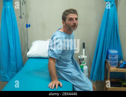 scared and worried man hospitalized - attractive injured man sitting on hospital bed receiving treatment feeling sick and unwell after suffering accid Stock Photo