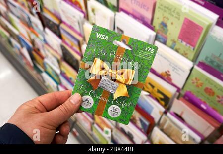 Montreal, Canada - May 03, 2020: Visa gift card in a hand over a stand with gift cards. Visa is an American multinational financial services corporati