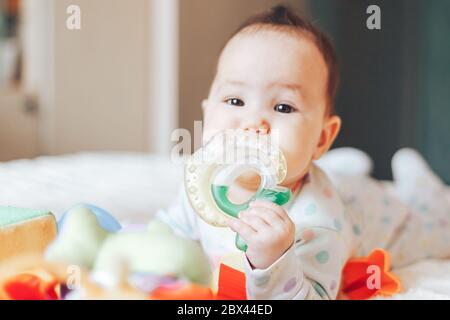 Portrait of a cute 6 month old baby, boy or girl, playing with a teething toy.
