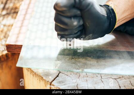 Cutting glass by glass cutter. Man hands with gloves holding glass cutter. Stock Photo