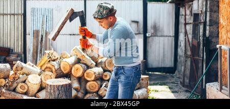 Man in jeans and checkered shirt standing near stump with ax in hands long banner Stock Photo