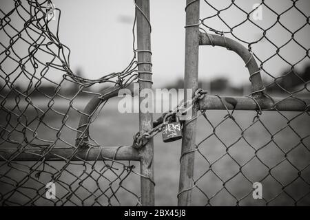 Padlocked chain around wire gate with hole in wire and graffiti on padlock Stock Photo