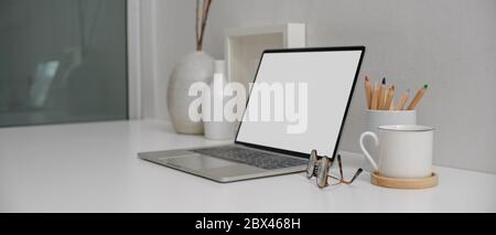 Cropped shot of modern workspace with mock-up laptop, painting tools, and decorations on white desk beside window Stock Photo
