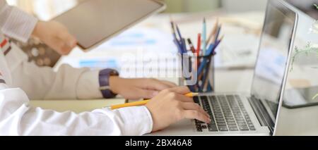 Side view of UI developer working on laptop with stationery and paperwork on white worktable Stock Photo