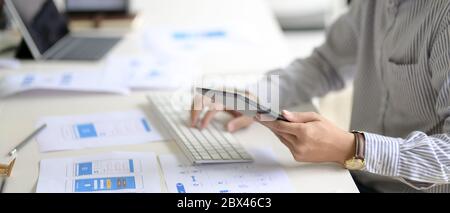 Side view of UI developer working with digital tablet, computer and paperwork on white office desk Stock Photo