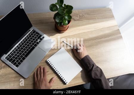 Mans hands, white paper notebook, pencil, laptop and plant on table Stock Photo