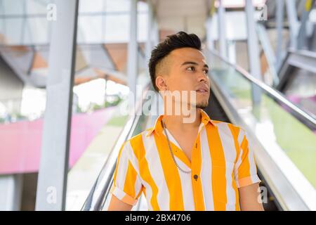 Young handsome multi ethnic man thinking while moving down the escalator in the city Stock Photo