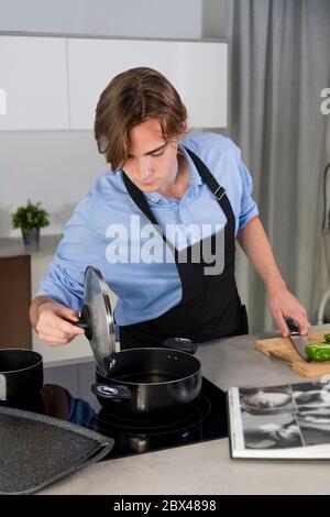Handsome young man checking a pot at a kitchen on an out of focus background. Safety and cooking at home concept.po Stock Photo