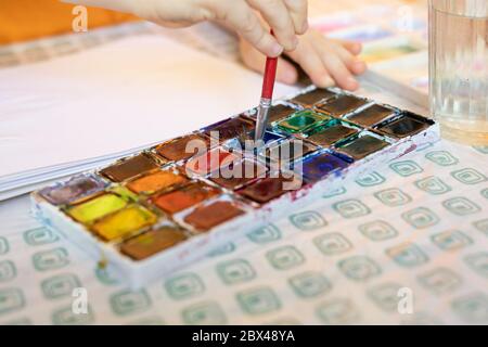 Close up of child engaged in artwork with colorful mixed paints and brushes. Stock Photo