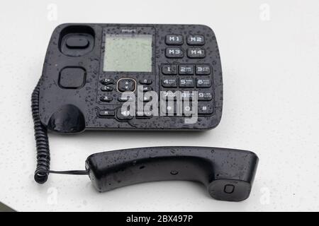 Black desktop telephone with rain drops on white table. Retro, dialing, connection, communication, office equipment. Russia, Bashkortostan, July 2019. Stock Photo