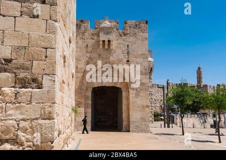 a lone masked policeman walking past the jaffa gate of the old city of jerusalem with the tower of david in the background during quarantine Stock Photo