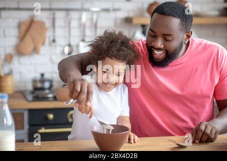 African american bearded man stirring milk in his daughters plate Stock Photo