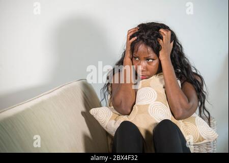 young attractive and sad black African American woman sitting depressed at home sofa couch feeling anxious and frustrated suffering menstruation perio Stock Photo