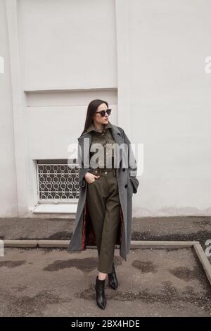 looking confusedly down. Photo of a young lady in fashionable clothes in full growth on minimalistic urban background. Concept of fashion Stock Photo