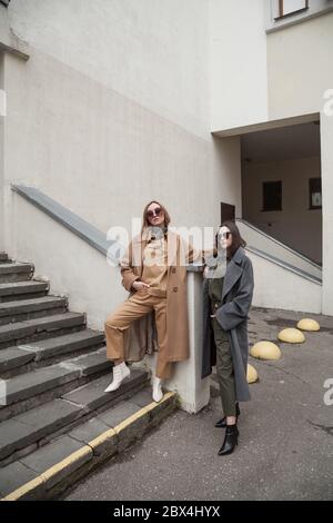 Fashion portrait of Two stylish pretty women posing on the street in cloudy day. Wearing trendy urban outfit , woolen coats and boots heels Stock Photo