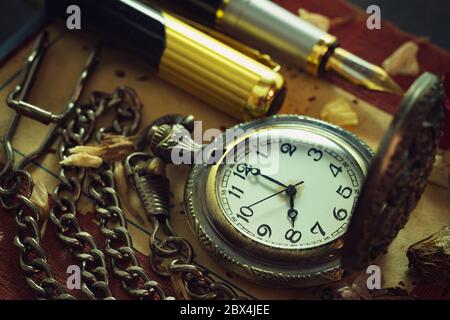 Vintage pocket watch and brass pen on old book. At 8 o'clock in morning. Education and vintage style concept. Stock Photo