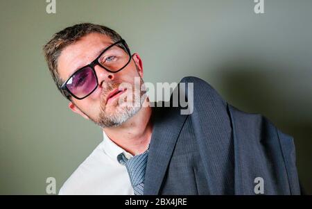 hilarious portrait of 40s weird and wasted businessman in suit and tie wearing ridiculous big broken nerdy glasses posing exhausted feeling a loser is Stock Photo