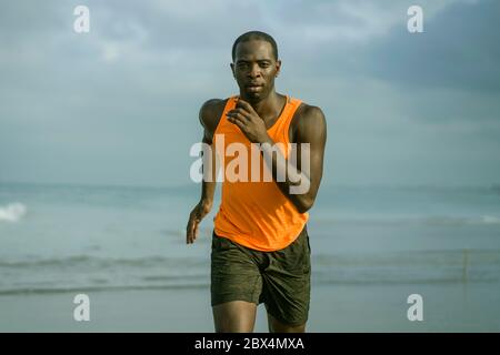 young attractive and fit black afro American man running on the beach doing Summer fitness jogging workout at the sea in sport exercise and healthy li Stock Photo