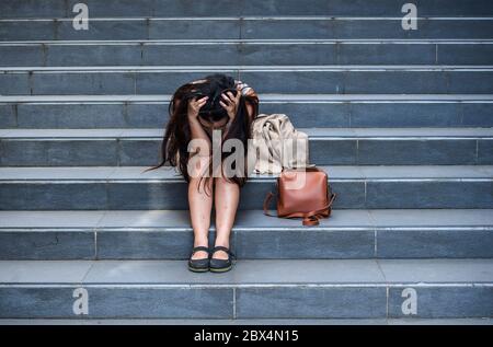 young depressed and desperate business woman crying alone sitting on street staircase suffering stress and depression crisis being victim of mobbing o Stock Photo