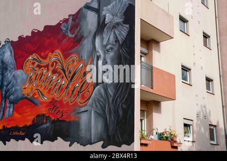 05 June 2020, Baden-Wuerttemberg, Mannheim: A mural by the Mannheim graffiti artist Rick Riojas shows a motif of a girl holding the hand of an elderly person on the façade of a house in the Schönau district. The lettering 'Family is everything' is sprayed in between. Riojas artworks, which are applied to houses of the Mannheim housing association GBG, will only be on display for a certain period of time until the buildings are renovated. Photo: Uwe Anspach/dpa - ATTENTION: Only for editorial use in connection with a report on murals on house facades of the Mannheimer Wohnungsbaugesellschaft GB Stock Photo