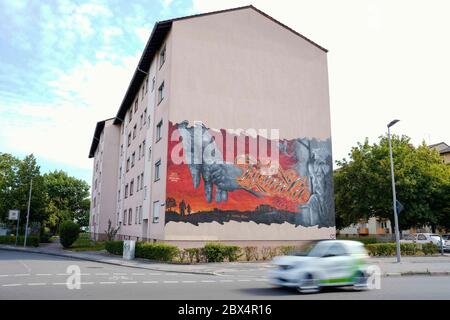 05 June 2020, Baden-Wuerttemberg, Mannheim: A car drives past a house façade in the Schönau district with a mural by Mannheim graffiti artist Rick Riojas. The graffiti shows the motif of a girl holding the hand of an older person. The lettering 'Family is everything' is sprayed in between. Riojas works of art, which are applied to houses of the Mannheim housing association GBG, will only be visible for a certain time until the buildings are renovated. Photo: Uwe Anspach/dpa - ATTENTION: Only for editorial use in connection with a report on murals on house facades of the Mannheimer Wohnungsbaug Stock Photo