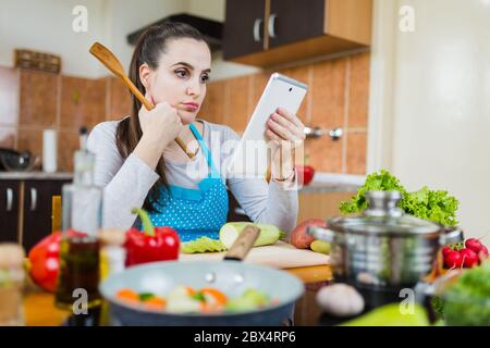 Young housewife learning to cook by watching online video recipe tutorial. Stock Photo
