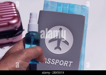 Hand holding passport,medical mask and sanitizer spray with suitcase on white background. Lifestyle concept in New Normal after Covid-19 pandemic. Stock Photo