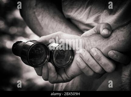 Man with work stained hands holding binoculars behind back. Stock Photo
