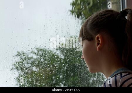 Girl looking through rain covered window Stock Photo